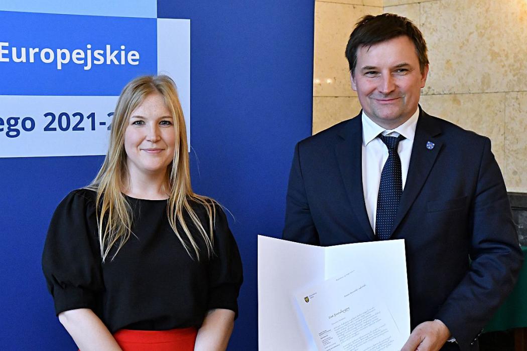 Uśmiechnieci kobieta i mężczyzna. Mężczyzna trzyma w rękach list gratulacyjny.