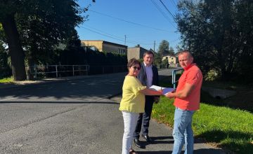 Trzy osoby stojące na skrzyżowaniu ulic. Jedna z nich podpisuje dokument.